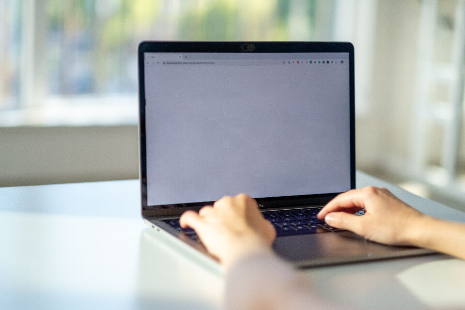 Hands typing on a laptop keyboard at a sunlit desk