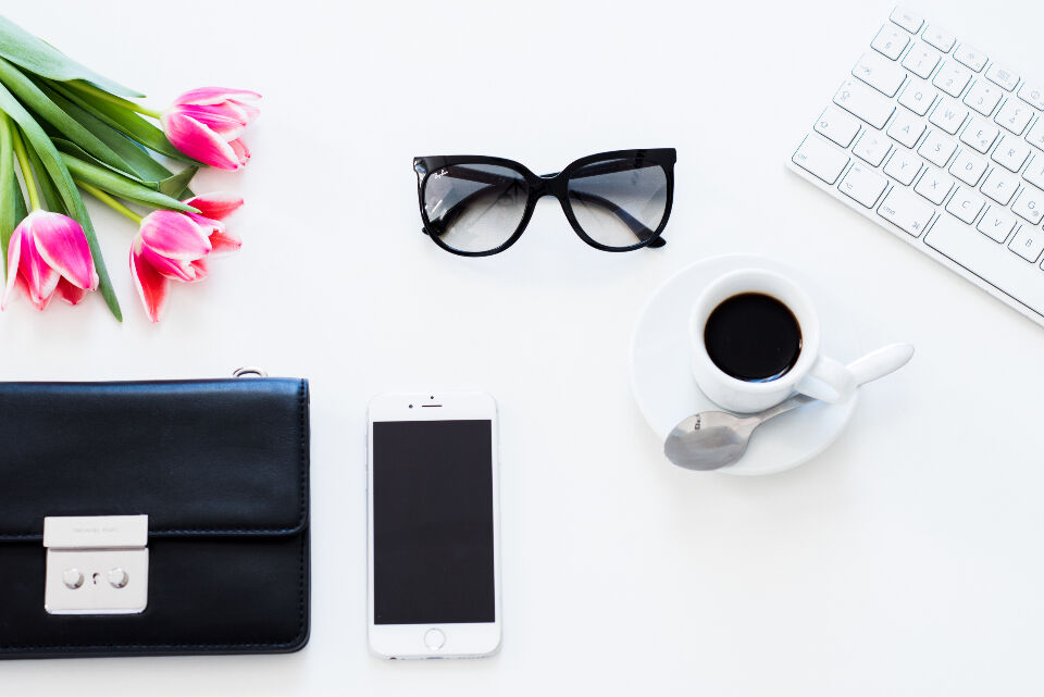 Flat lay of a minimalist desk with keyboard, phone, coffee and flowers