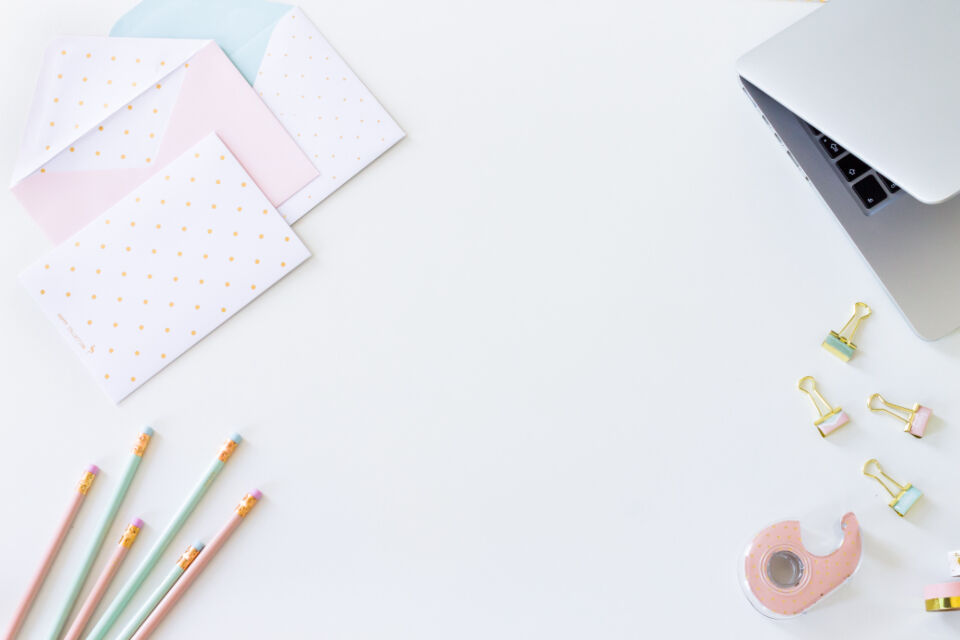 Flat lay of a clean, minimalist desk with a laptop, envelope and paperclip