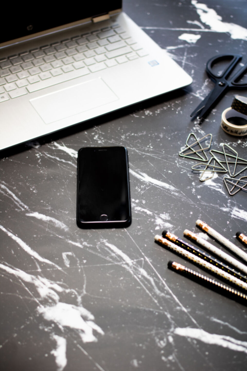 Laptop and phone on a marble table with craft supplies